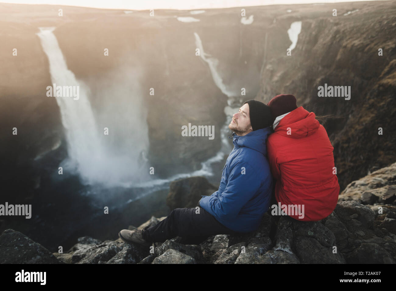 Randonneur couple sitting on cliff par Haifoss cascade en Islande Banque D'Images