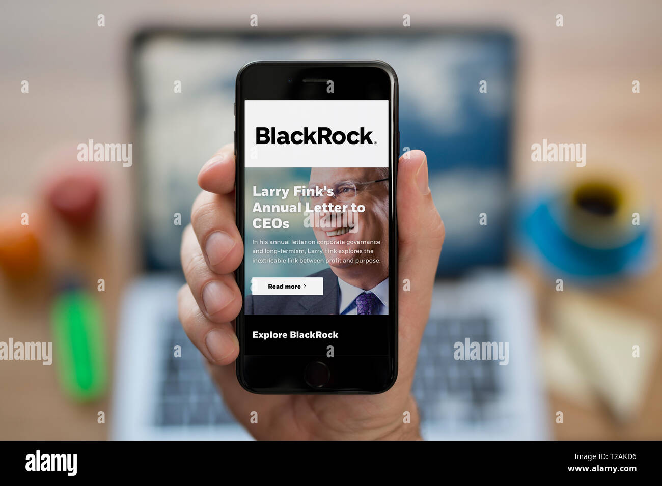 Un homme se penche sur son iPhone qui affiche le logo de BlackRock (usage éditorial uniquement). Banque D'Images