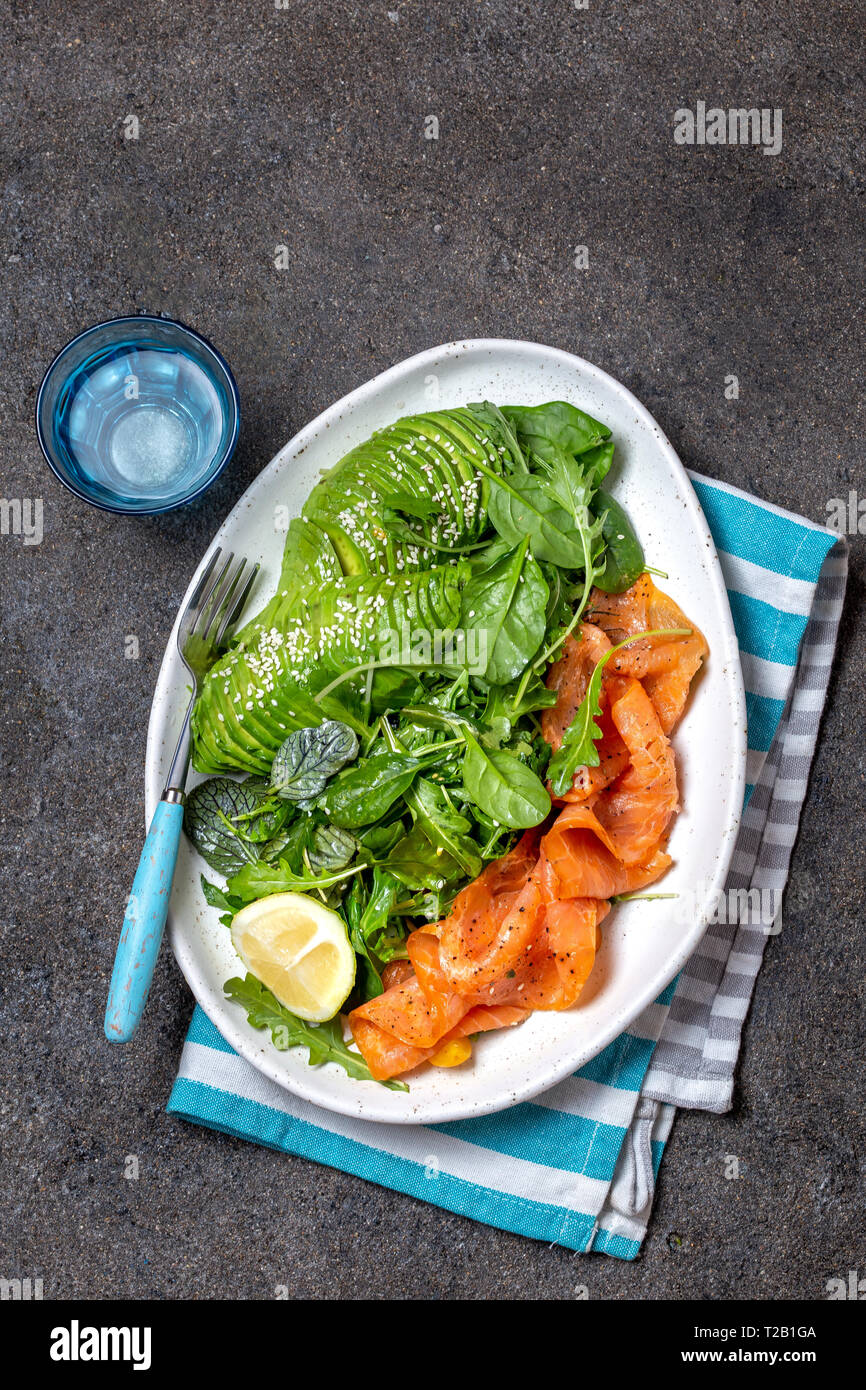 Glucides faible salade. Les épinards, salade de roquette à l'avocat et le saumon. Arrière-plan de béton noir, plaque blanche, vue du dessus Banque D'Images