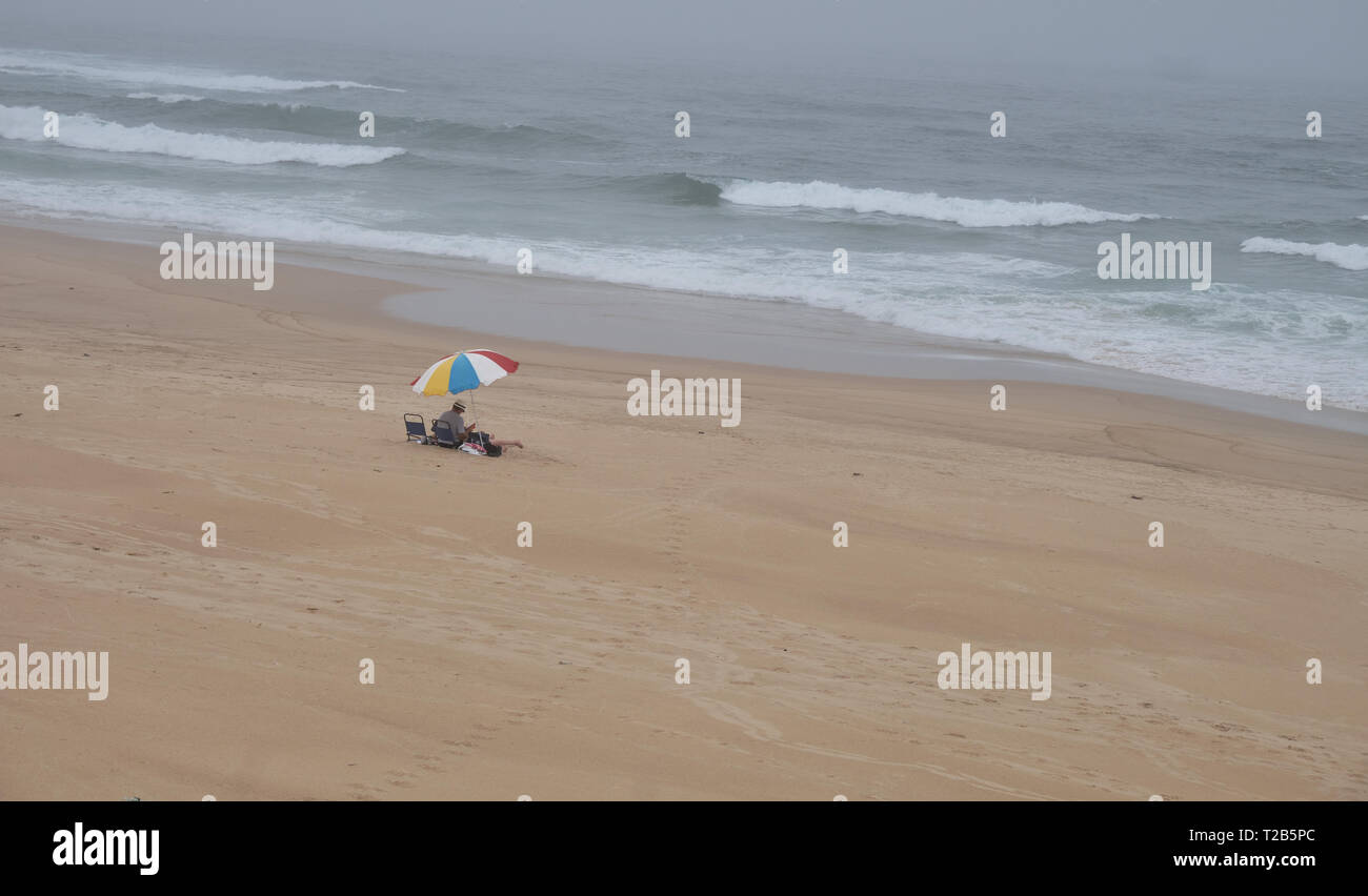 Plage avec un seul et même sur une journée d'automne. Capture de désolation, avec seulement quelques couple visible sous le parapluie Banque D'Images