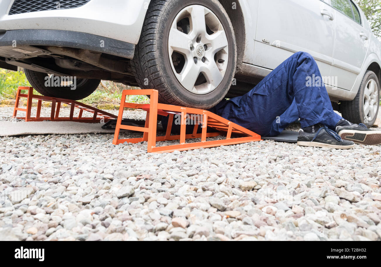 Jeune homme étendu sous sa voiture a augmenté vers le haut sur des rampes Banque D'Images