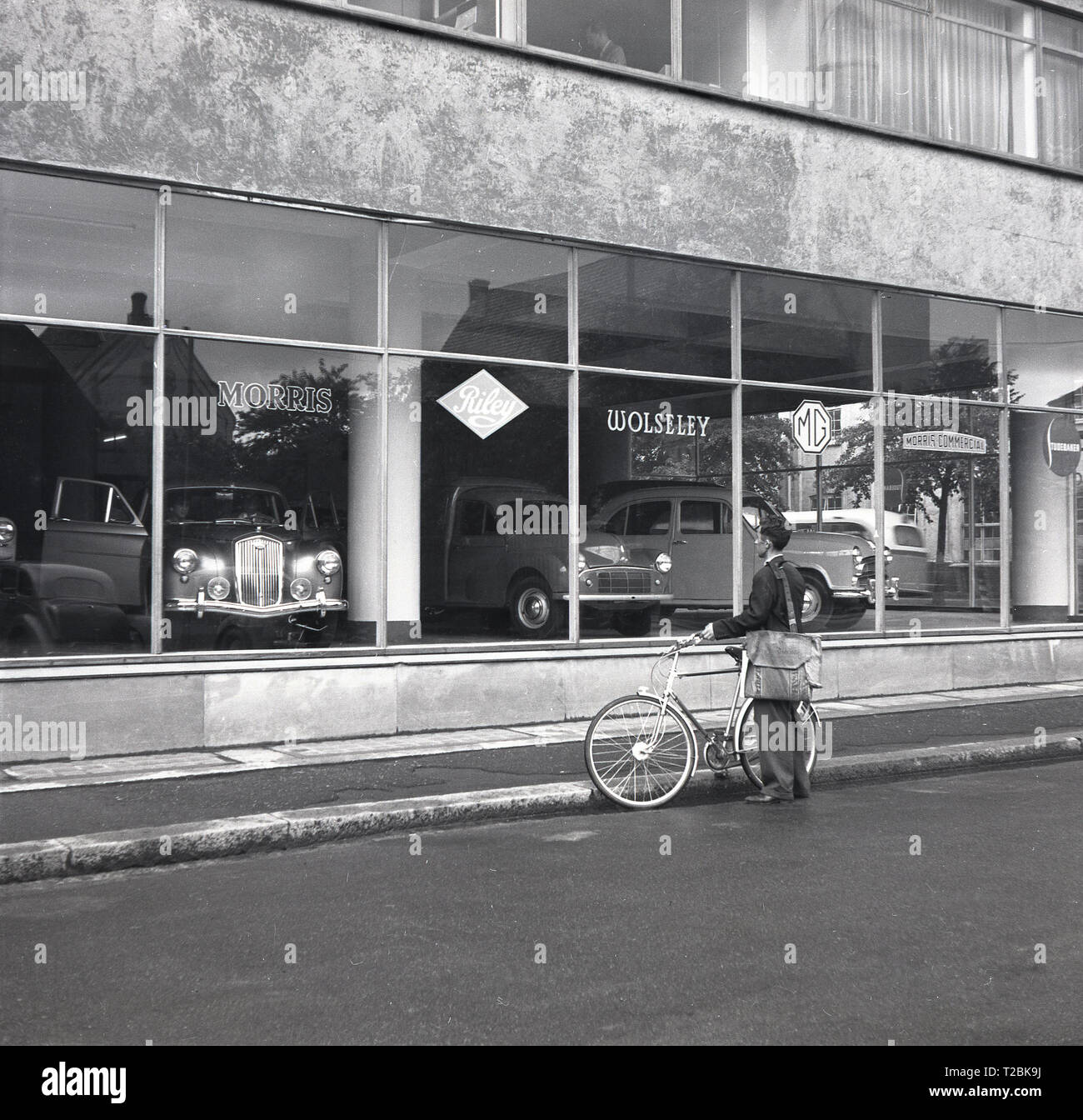 Années 1950, historiques, l'homme avec une sacoche debout près de son vélo dans une rue à l'intérieur d'une voiture à l'Austin Morris car showroom, la Norvège. Banque D'Images