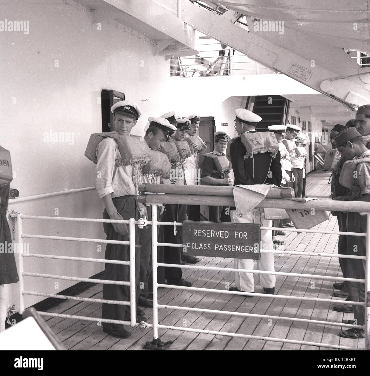 Années 1950, historique, l'équipage d'un navire sur le pont du navire à vapeur P & O SS Chusan se préparant à un exercice de sécurité ou à un exercice d'entraînement avec leur gilet de sauvetage, dans la zone réservée aux passagers de première classe. Un paquebot construit pour les lignes P & O Orient voyageant en Inde et en extrême-Orient, elle a été nommée d'après Chusan, une petite île au large de la Chine. Banque D'Images