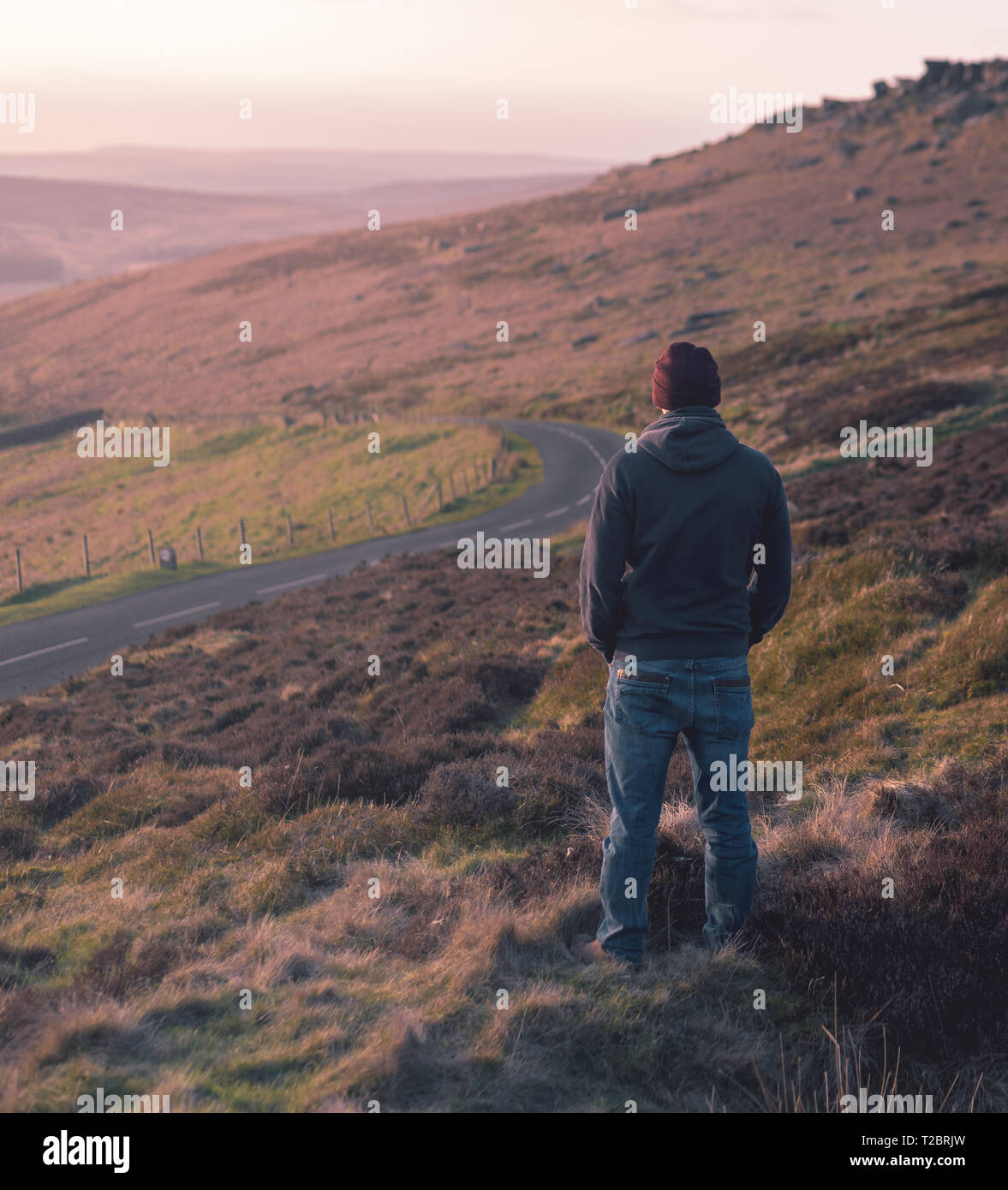 Un homme seul dans un hoody, jeans et chapeau regarde un beau coucher de soleil rose dans le parc national de Peak District - UK - Printemps 2019 Banque D'Images