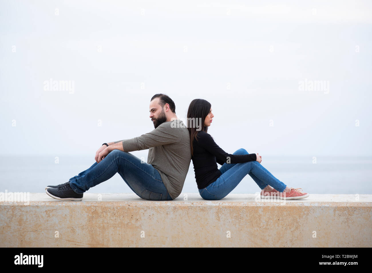 Mand et femme assise dos à dos sur la plage Banque D'Images