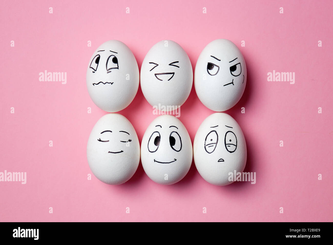 Oeufs de Pâques en compagnie de drôles d'expressions faciales. Les œufs avec différents visages sur fond rose. Banque D'Images