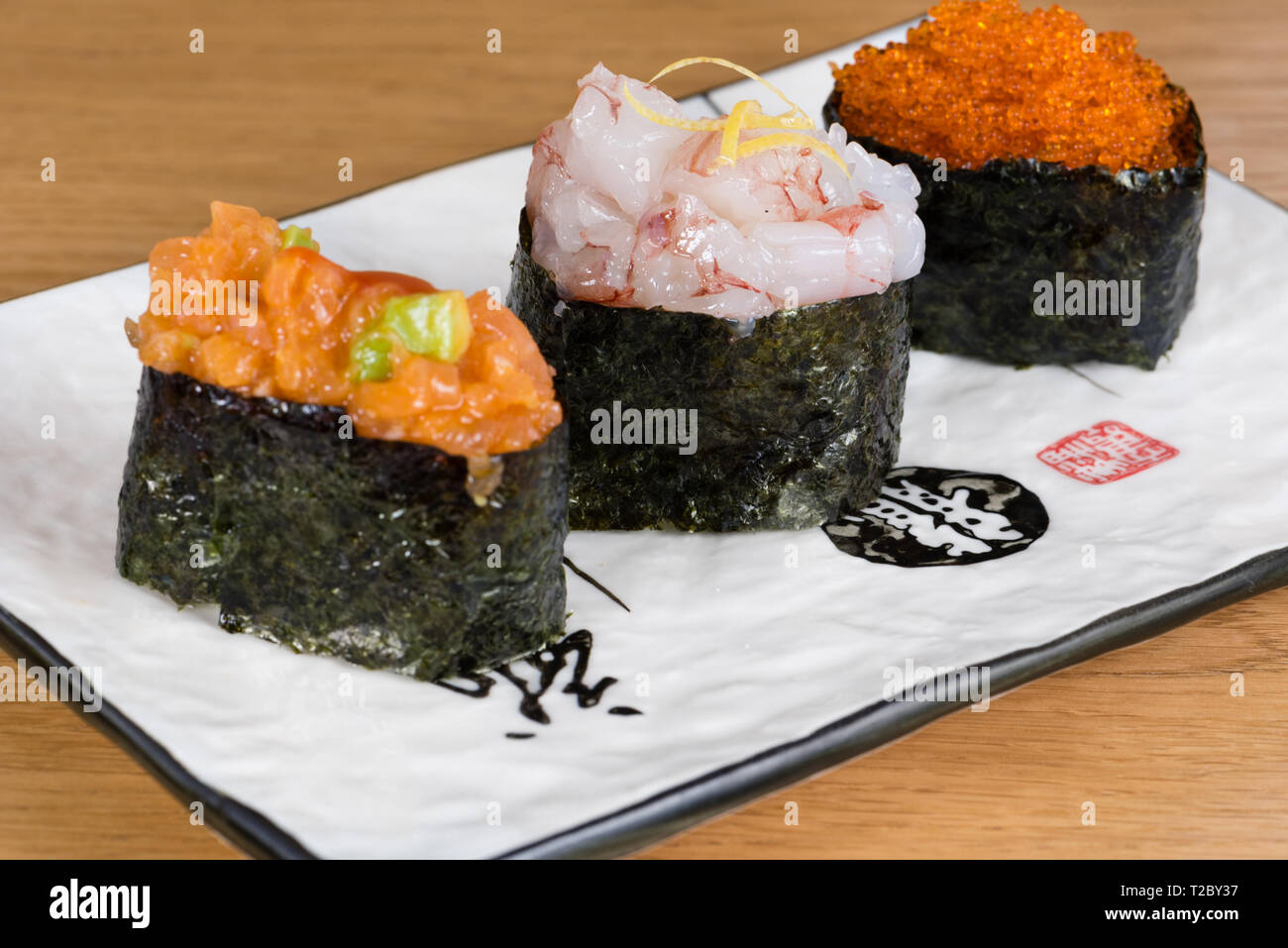 Mélange de gunkan tartare d'avocat et de saumon, de crevettes et de viande d'écorce de citron et caviar enveloppée d'algue nori, servis sur une plaque rectangulaire Banque D'Images
