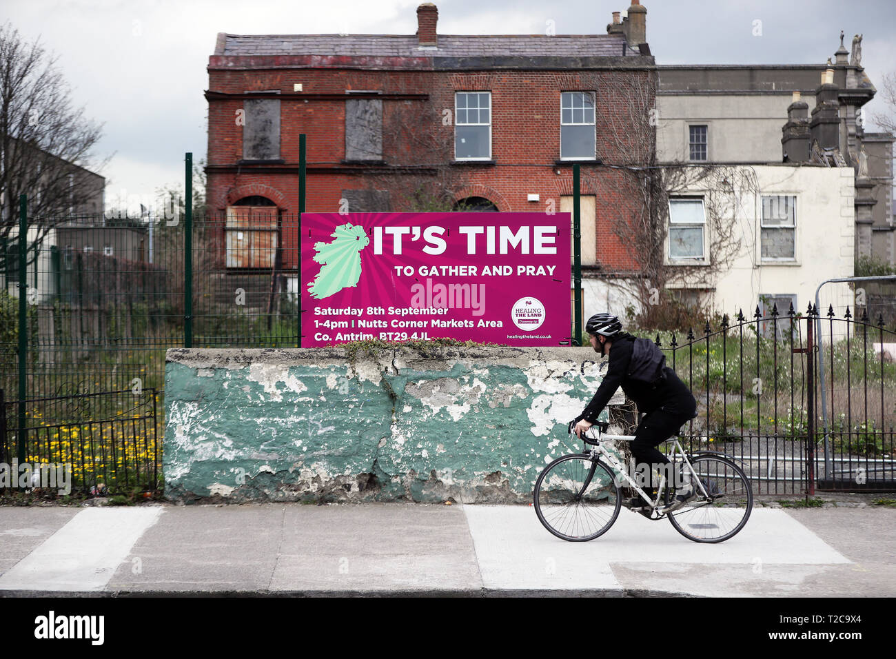 Un cycliste passe une publicité signe une réunion de prière en face de certaines maisons abandonnées sur Jones Road, à Dublin, Irlande. Banque D'Images