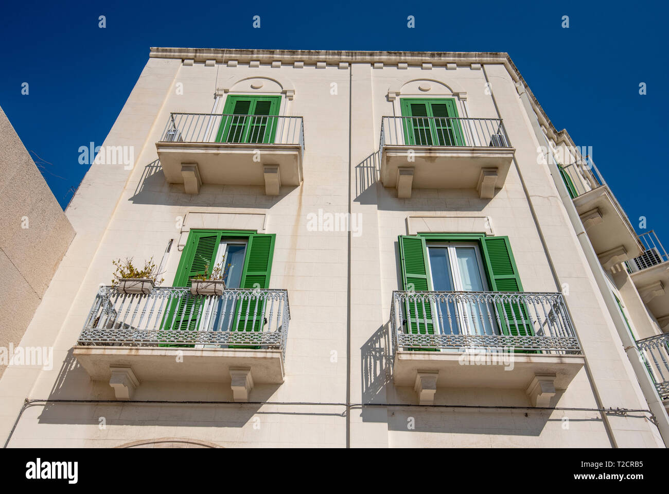 Vue frontale d'un vert en bois fenêtres sur mur jaune. Beau balcon. L'extérieur d'un logement dans la région de Bari, Pouilles, Italie. Région des Pouilles Banque D'Images