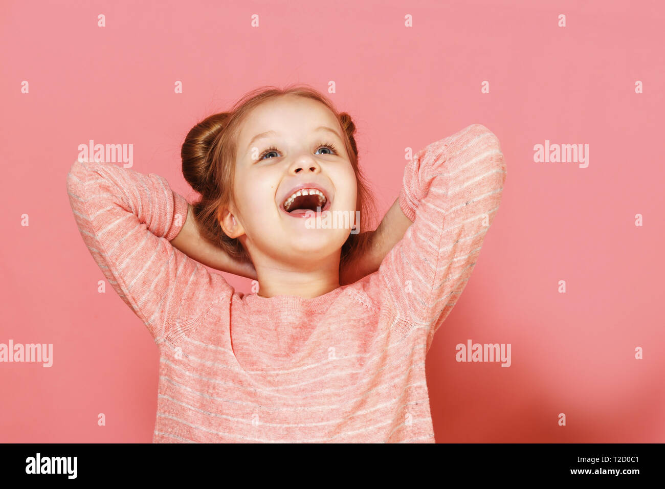 Closeup portrait of a cute little girl avec brins de cheveux sur fond rose. L'enfant a mis ses mains derrière sa tête jusqu'à rêveur. Banque D'Images