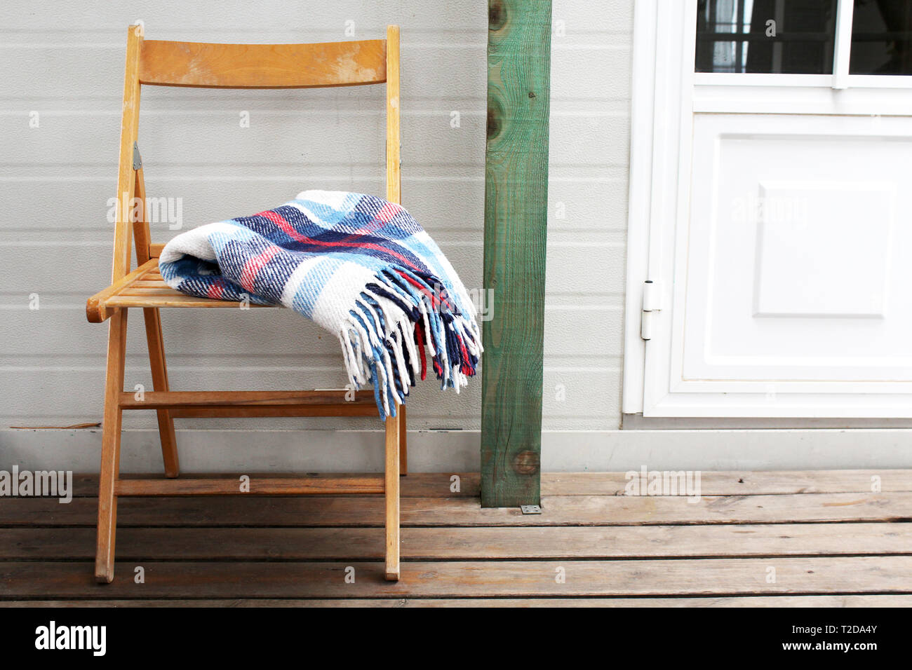 Une chaise en bois avec une couverture sur une véranda en face de la maison Banque D'Images