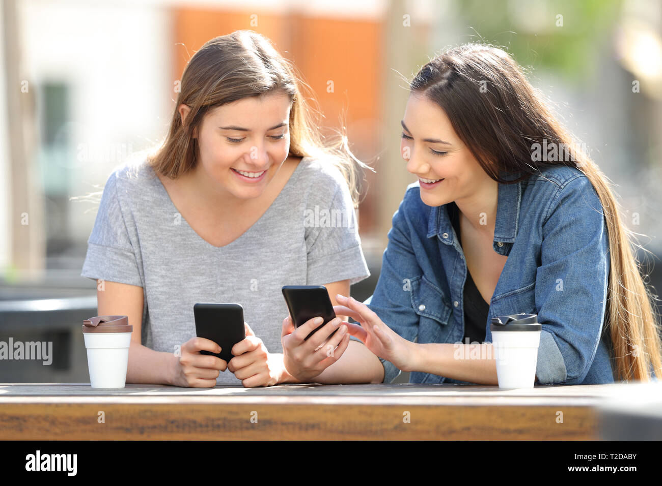 Deux amis heureux en comparant leurs téléphones intelligents assis dans un parc Banque D'Images