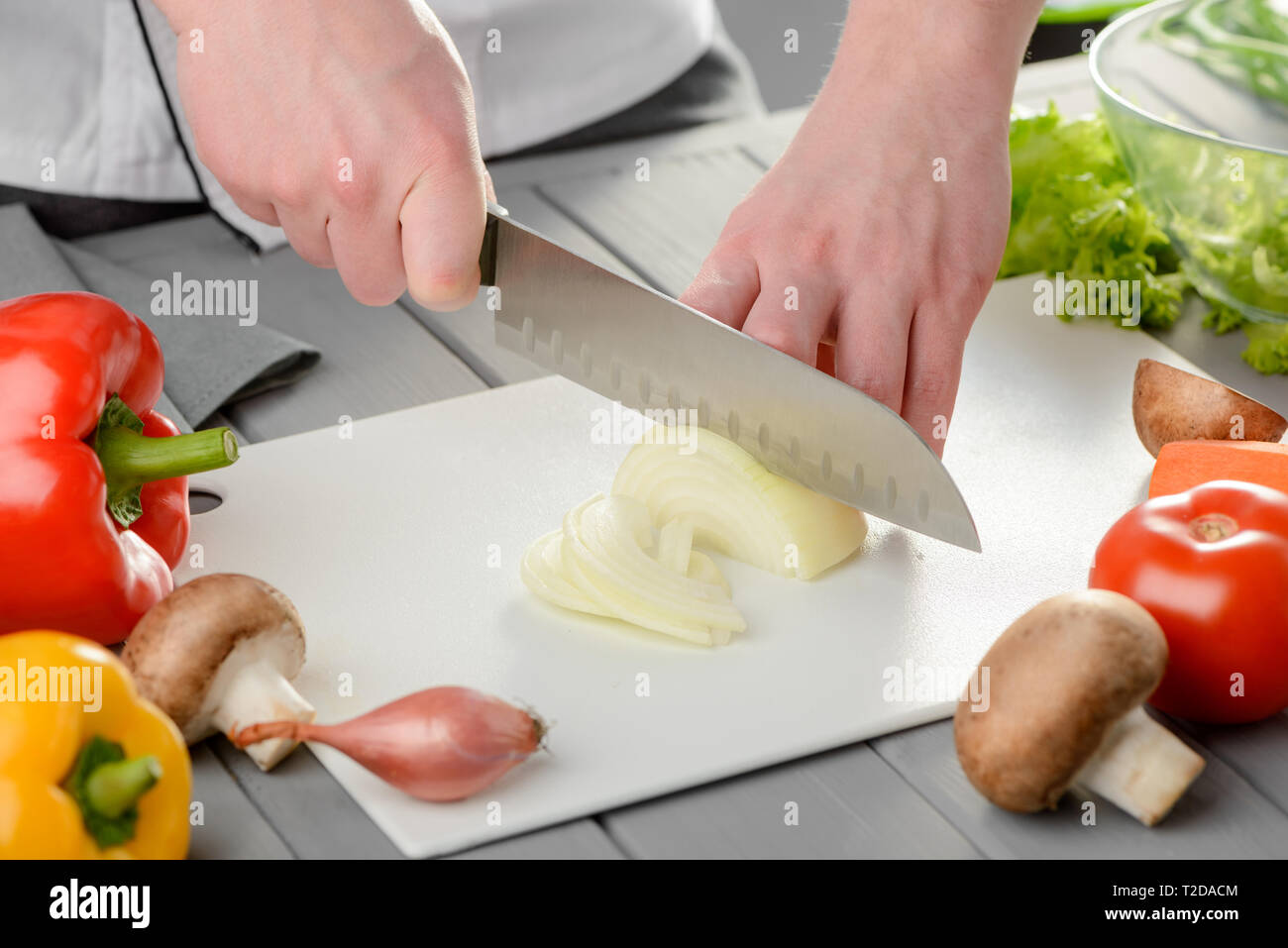 La coupe d'un homme de la moitié de l'oignon d'une ampoule en bandes. Bon couteau et divers technique légumes. La préparation d'aliments sains. Banque D'Images