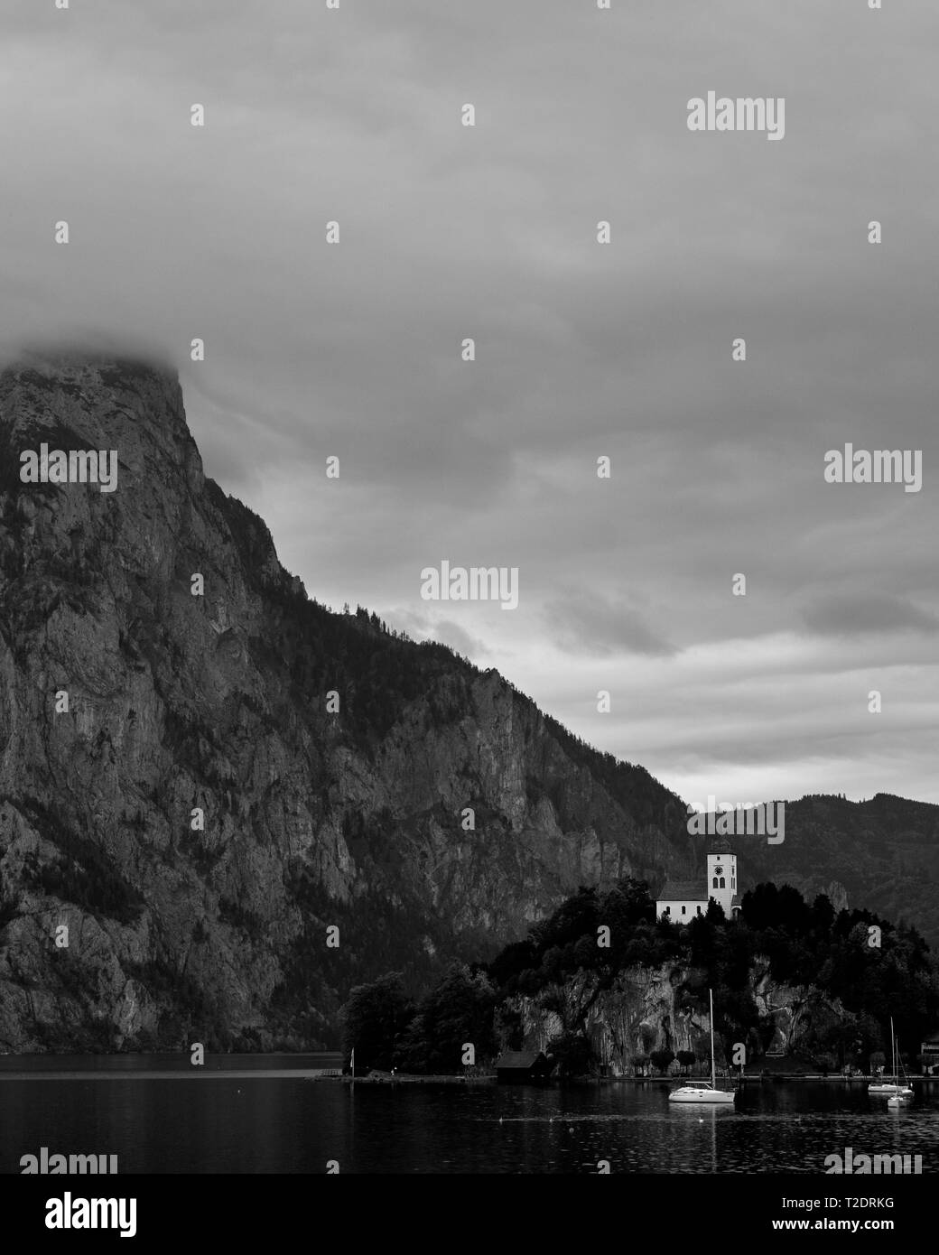 Vintage noir et blanc vue sur lac Alpes autrichiennes. Bateaux, yachts en face de l'église sur le rocher avec des nuages sur les Alpes montagne à Traunstein lak Banque D'Images