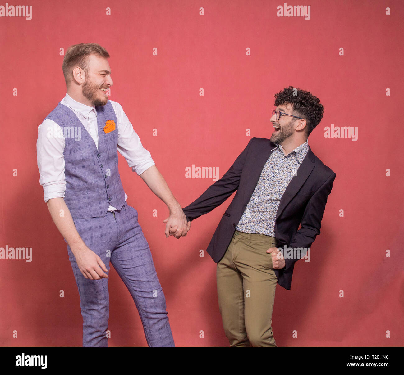 Deux hommes, trop quitté tout en tenant la main couple gay photo-shoot en studio (fond rose). regarder, face à face. smiling, HAP Banque D'Images
