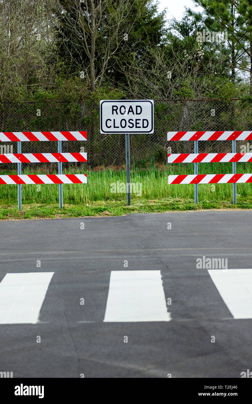 Shot verticale de deux barrières à rayures rouges et blanches avec une route fermée signe au milieu d'eux. Banque D'Images