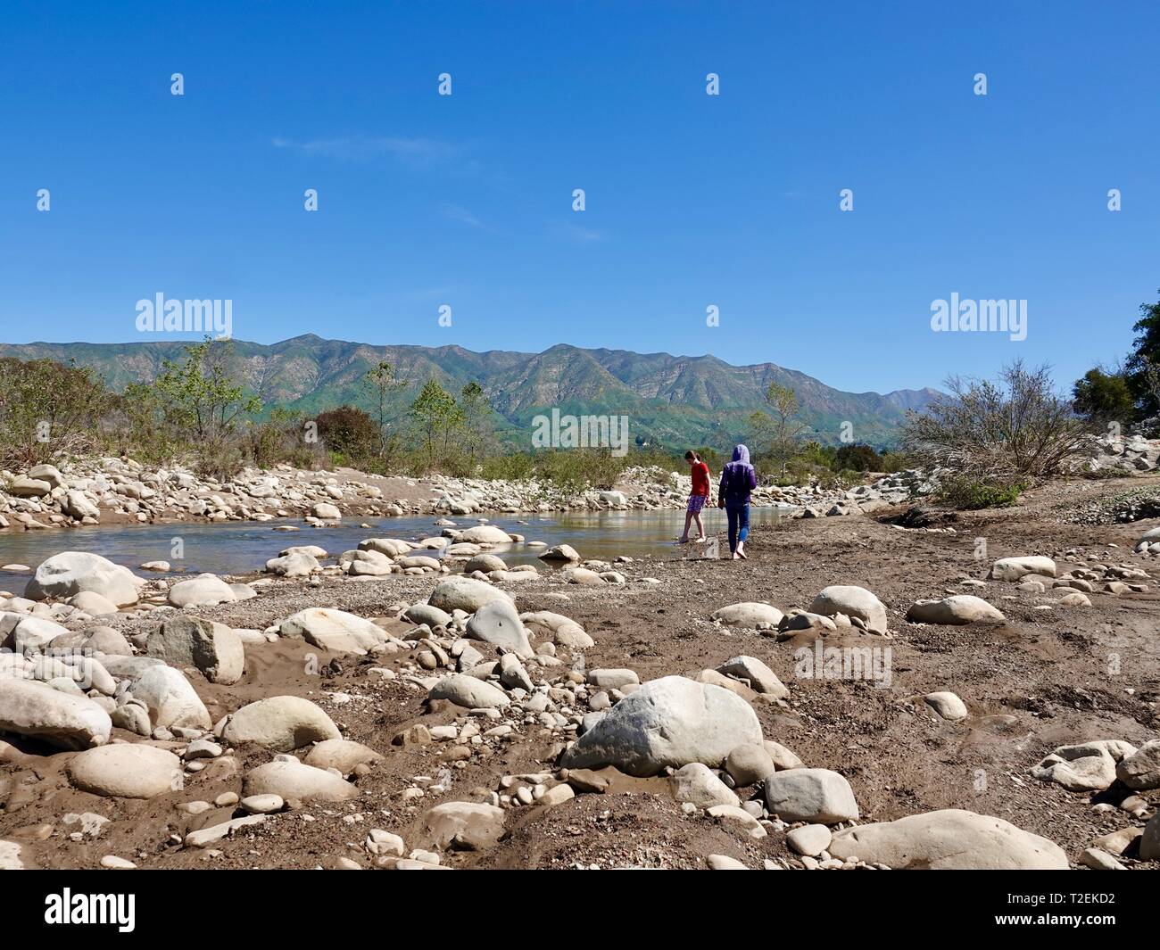 Deux jeunes filles, sœurs, jouant le long des rives de la rivière Ojai, sur une belle journée de printemps avec des montagnes et une végétation luxuriante, Ojai, Californie, USA Banque D'Images