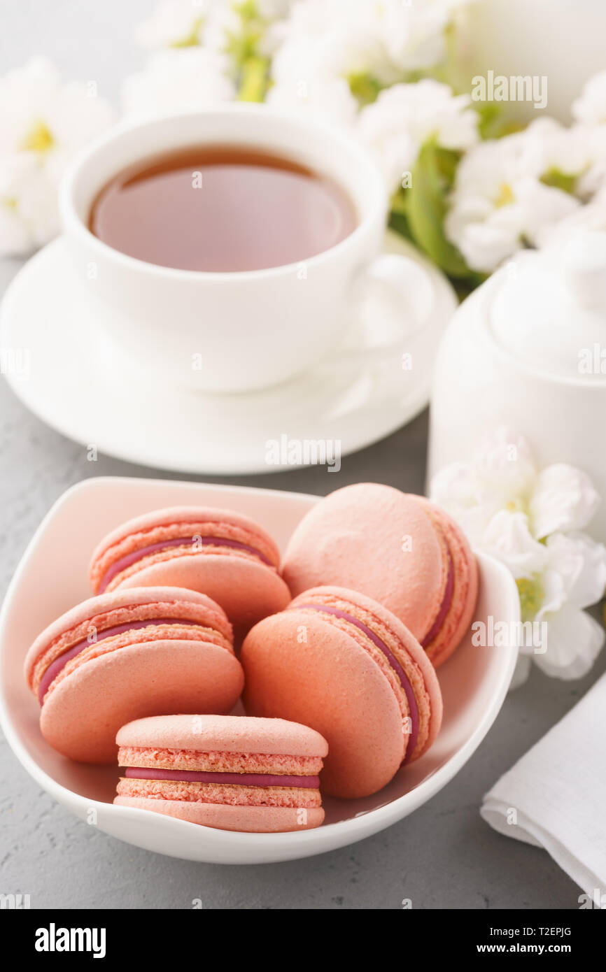 Macarons français rose avec berry le remplissage et un plateau pour le dessert. Fleurs dans l'arrière-plan. Banque D'Images