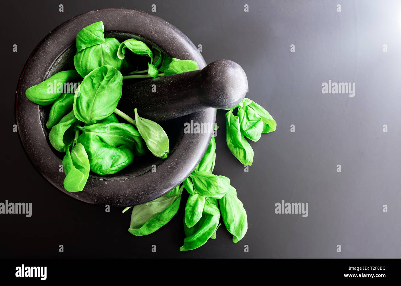 Vue de dessus de feuilles de basilic frais dans la pierre Mortier avec pilon sur comptoir de cuisine sombre Banque D'Images