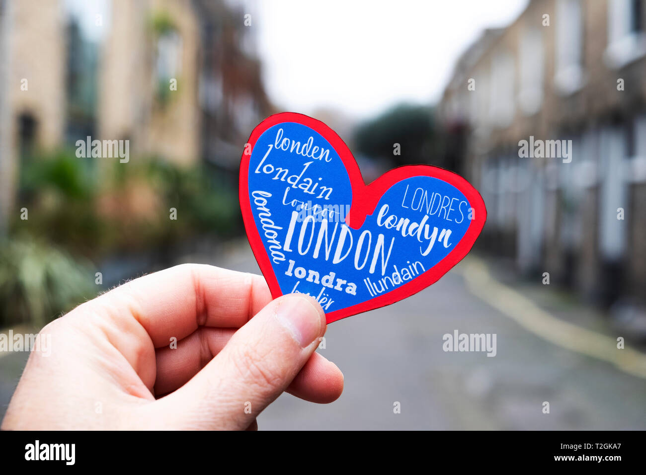 Libre de la main d'un jeune homme de race blanche, tenant un cœur avec le mot Londres en différentes langues, dans une vieille rue d'un immeuble d'neighborh Banque D'Images