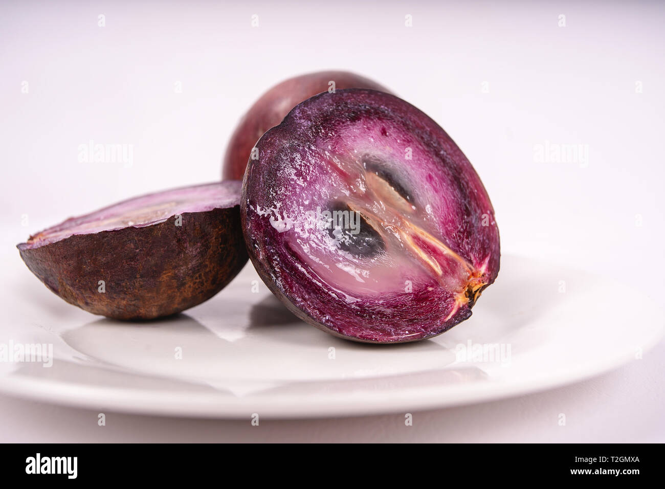 Deux fruits caimito sur une plaque, l'un d'entre eux coupé en deux pièces Banque D'Images
