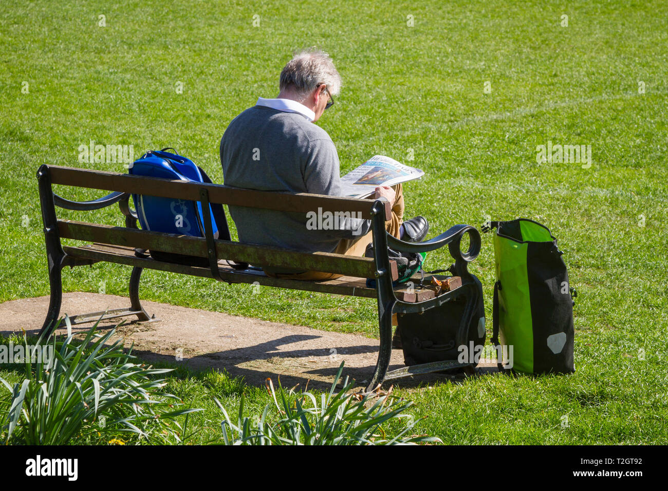 Un homme de l'âge de la retraite est assise au soleil sur un banc de parc lire le journal The Times en Semois Park, Oxford, UK Banque D'Images