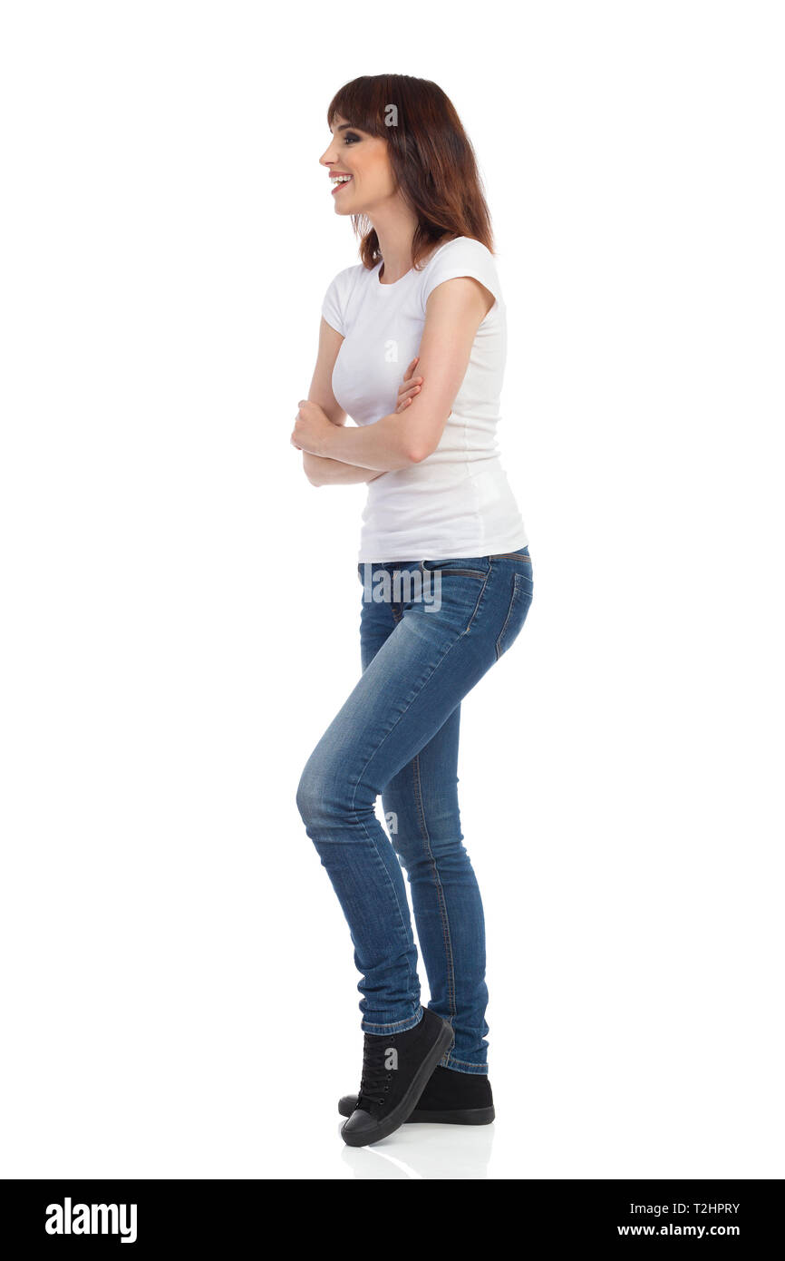 Jeune femme en jeans et t-shirt blanc est debout avec arma croisés, à l'écart et souriant. Studio pleine longueur shot isolé sur blanc. Banque D'Images