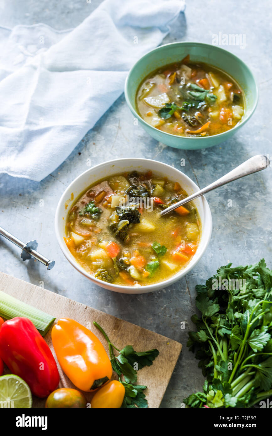 Minestrone, sur la Cuvette et pot de légumes couper sur une cutboard tomate cerise, citron vert, brun sur un fond blanc en béton Banque D'Images