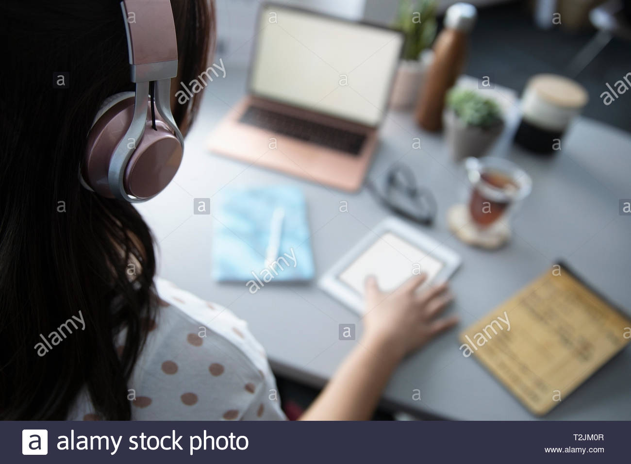 Woman with headphones using digital tablet at desk Banque D'Images