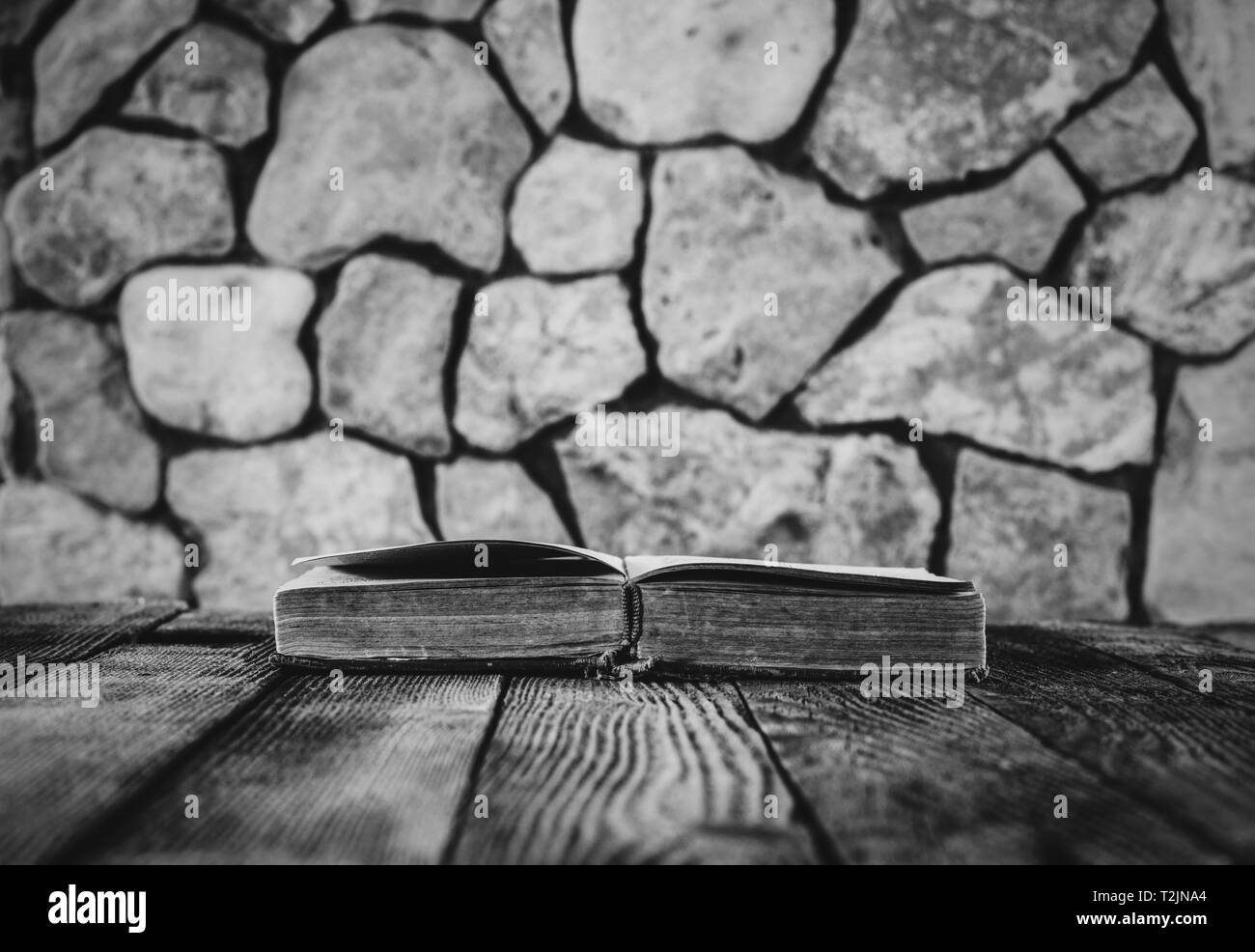 Vieux livre ouvert sur l'ancienne table en bois sur fond de murs en pierre. selective focus, photo noir et blanc. avec l'espace pour votre texte Banque D'Images