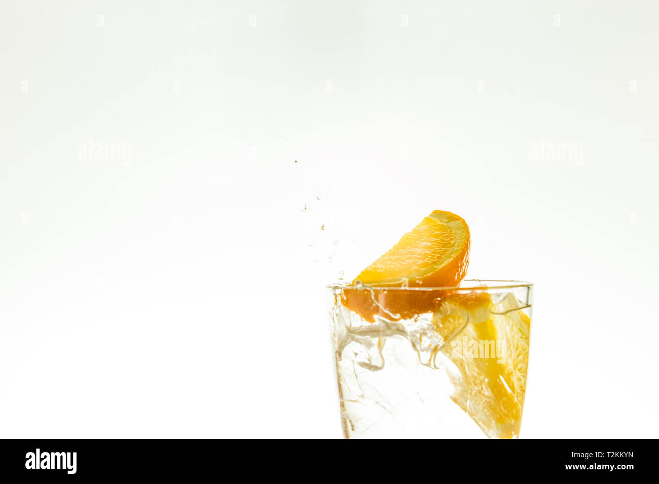 Couper les tranches d'orange dans un verre d'eau et faire un jet d'eau sur un fond blanc. l'eau pulvérisée dans l'air. Banque D'Images