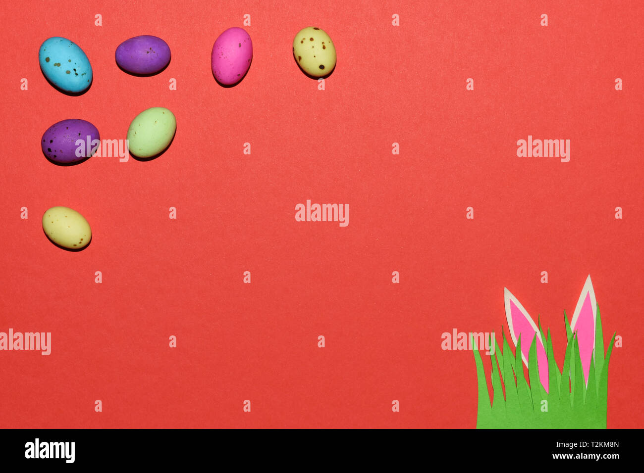 Candy Eggs With Grass Patch et oreilles de lapin sur rouge Banque D'Images