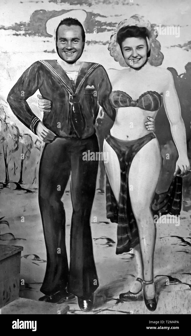 Vintage 1940 b&w face dans le trou photo d'un marin de la marine américaine avec sa petite amie à Coney Island, New York, USA. Banque D'Images