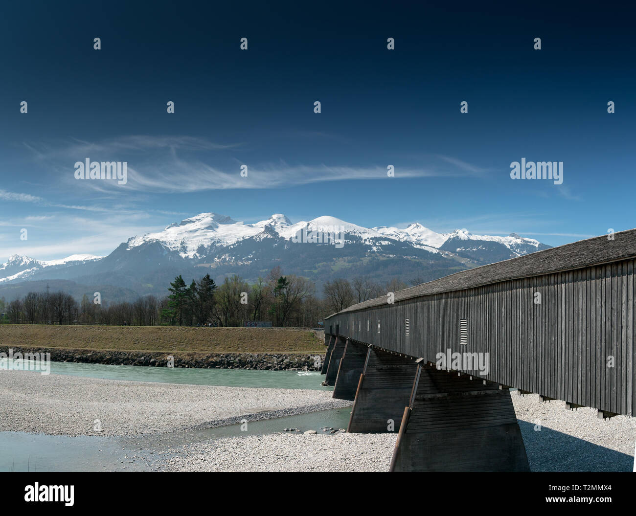 Vieux pont couvert en bois traversant le Rhin à partir de Liechtenstein à la Suisse avec une superbe vue sur les Alpes Suisses au printemps sous un ciel bleu Banque D'Images