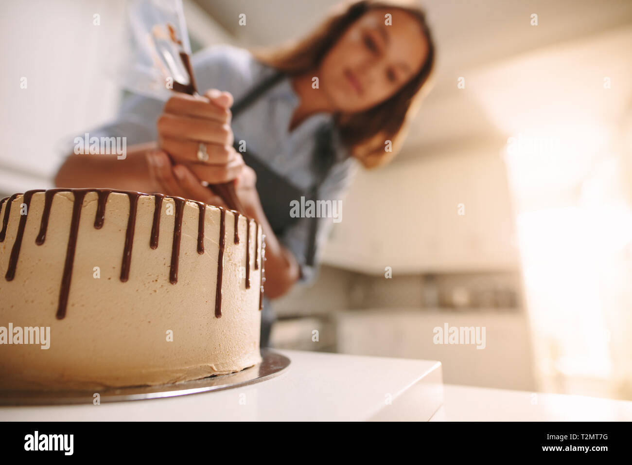 Gâteau sur un support en bois avec chef decorating en cuisine. Frais de décoration Baker délicieux gâteau fait maison avec du chocolat liquide sur la table. Banque D'Images