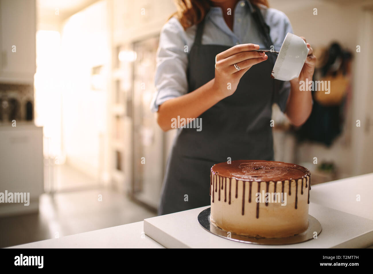 Chef pâtissier dans la cuisine Décorer un gâteau de chocolat. Femme en tablier pouring liquid sur un gâteau au chocolat sur comptoir de la cuisine. Banque D'Images