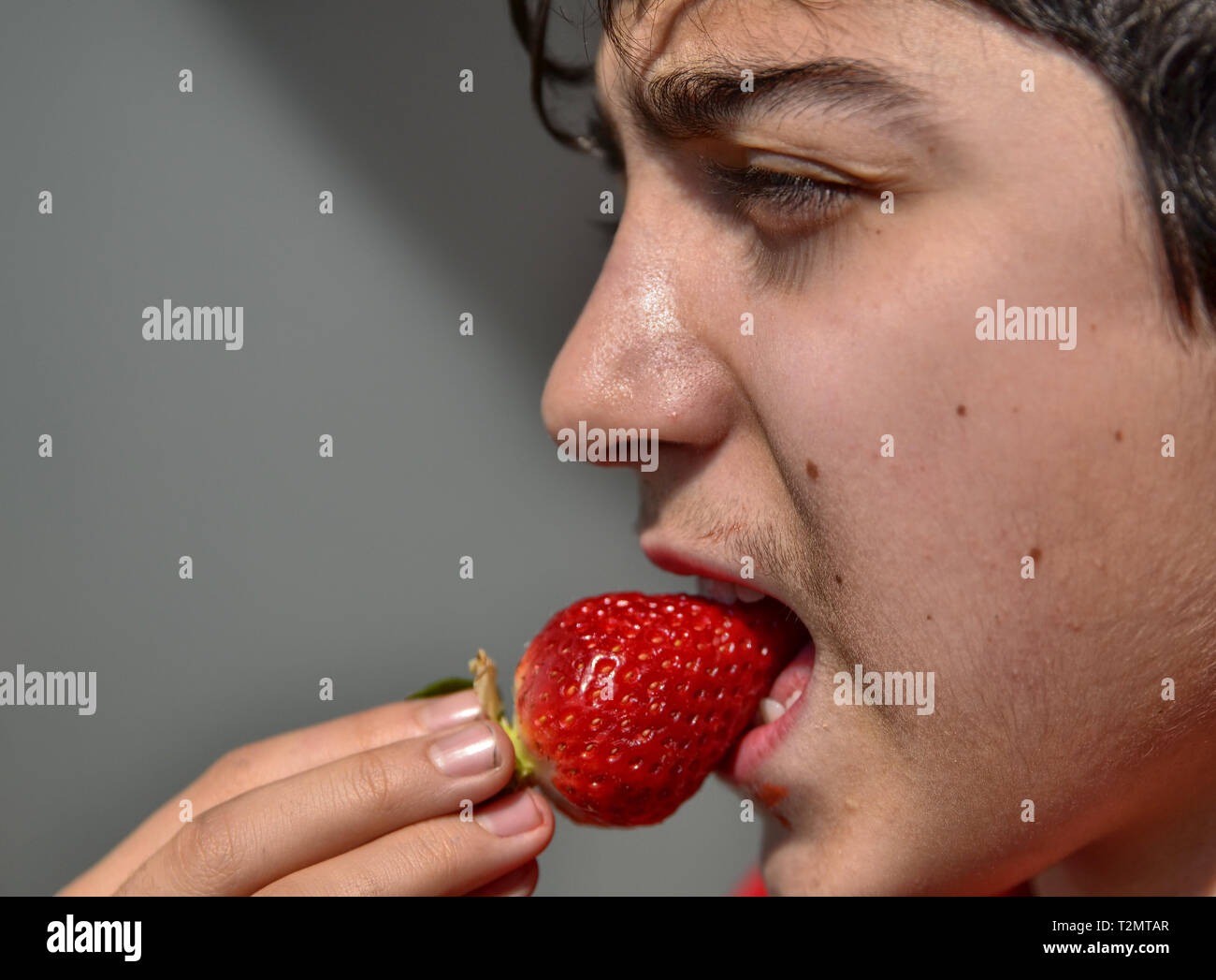 Close-up d'un caucasien enfant qui mange une fraise, le soleil intense entre le strabisme et renforcer le rouge vif des fruits. Banque D'Images