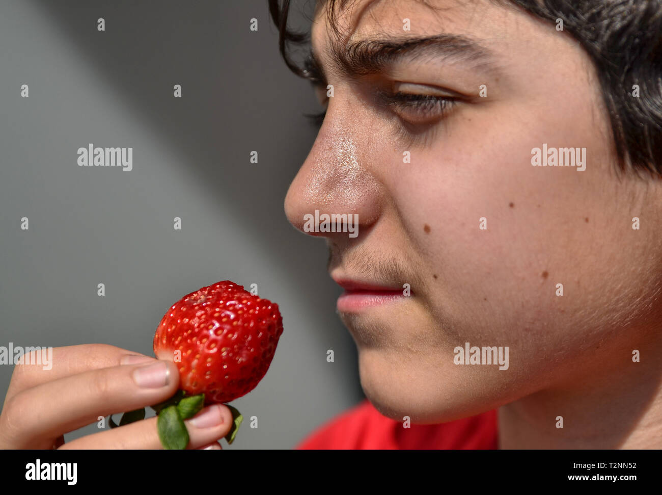Close-up d'un caucasien enfant qui mange une fraise, le soleil intense entre le strabisme et renforcer le rouge vif des fruits. Banque D'Images