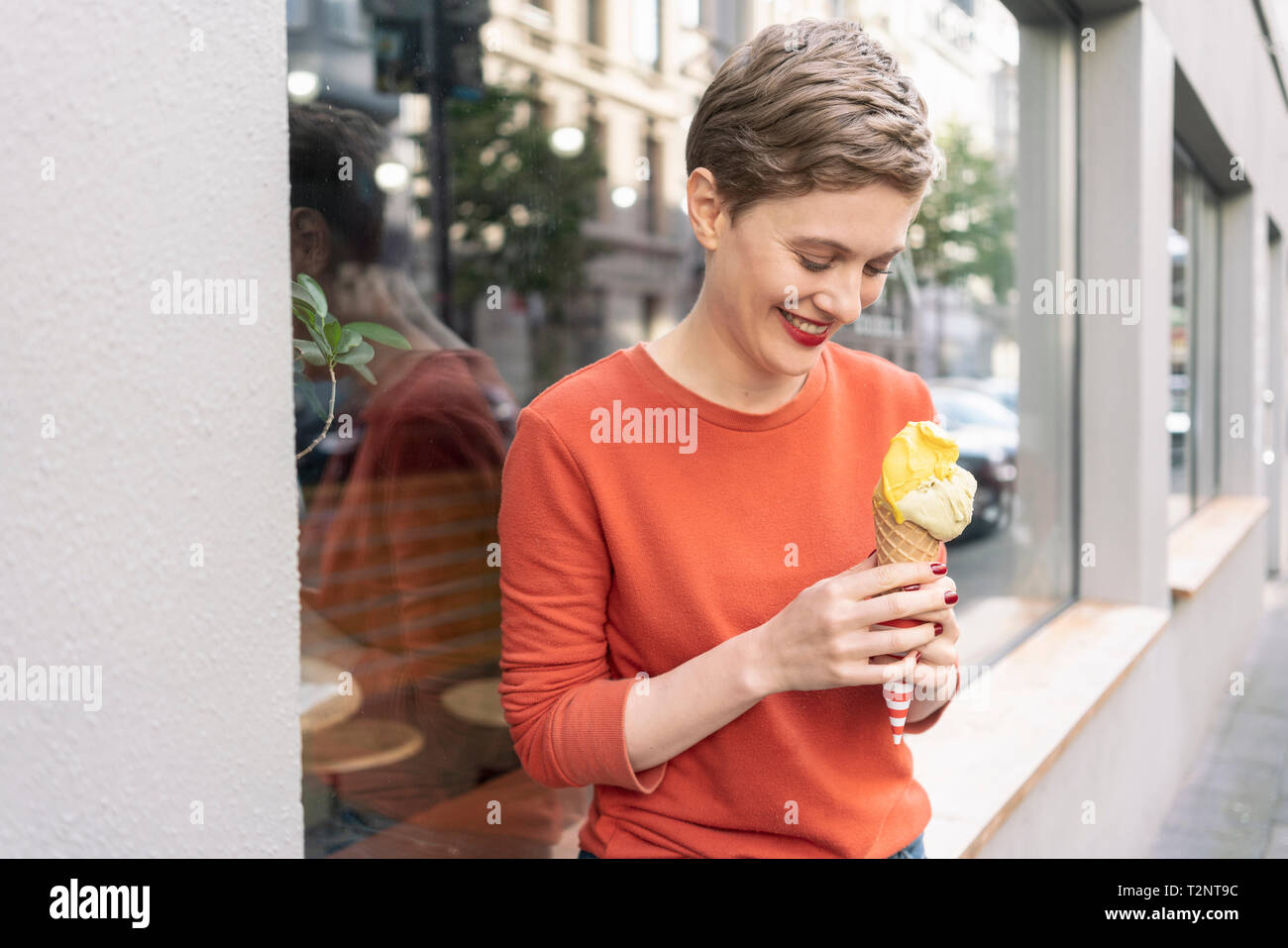 Woman eating ice cream en face de boutique, Cologne, Nordrhein-Westfalen, Allemagne Banque D'Images