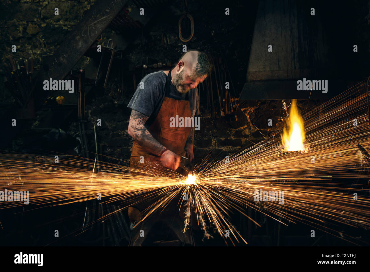 Mâle mature blacksmith hammering metal faire des étincelles sur enclume en atelier Banque D'Images