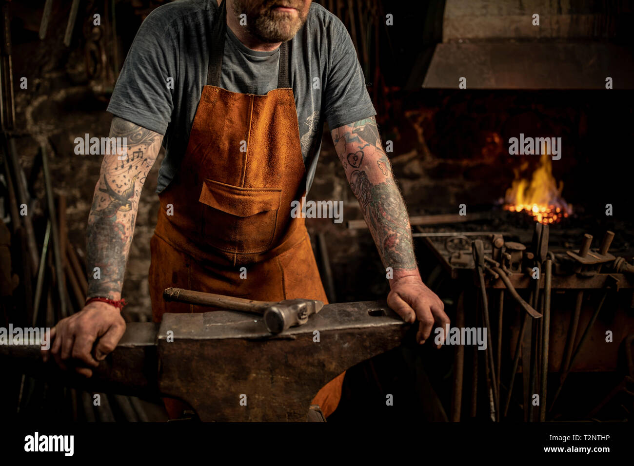 Mâle mature blacksmith appuyé contre anvil en atelier, cropped Banque D'Images