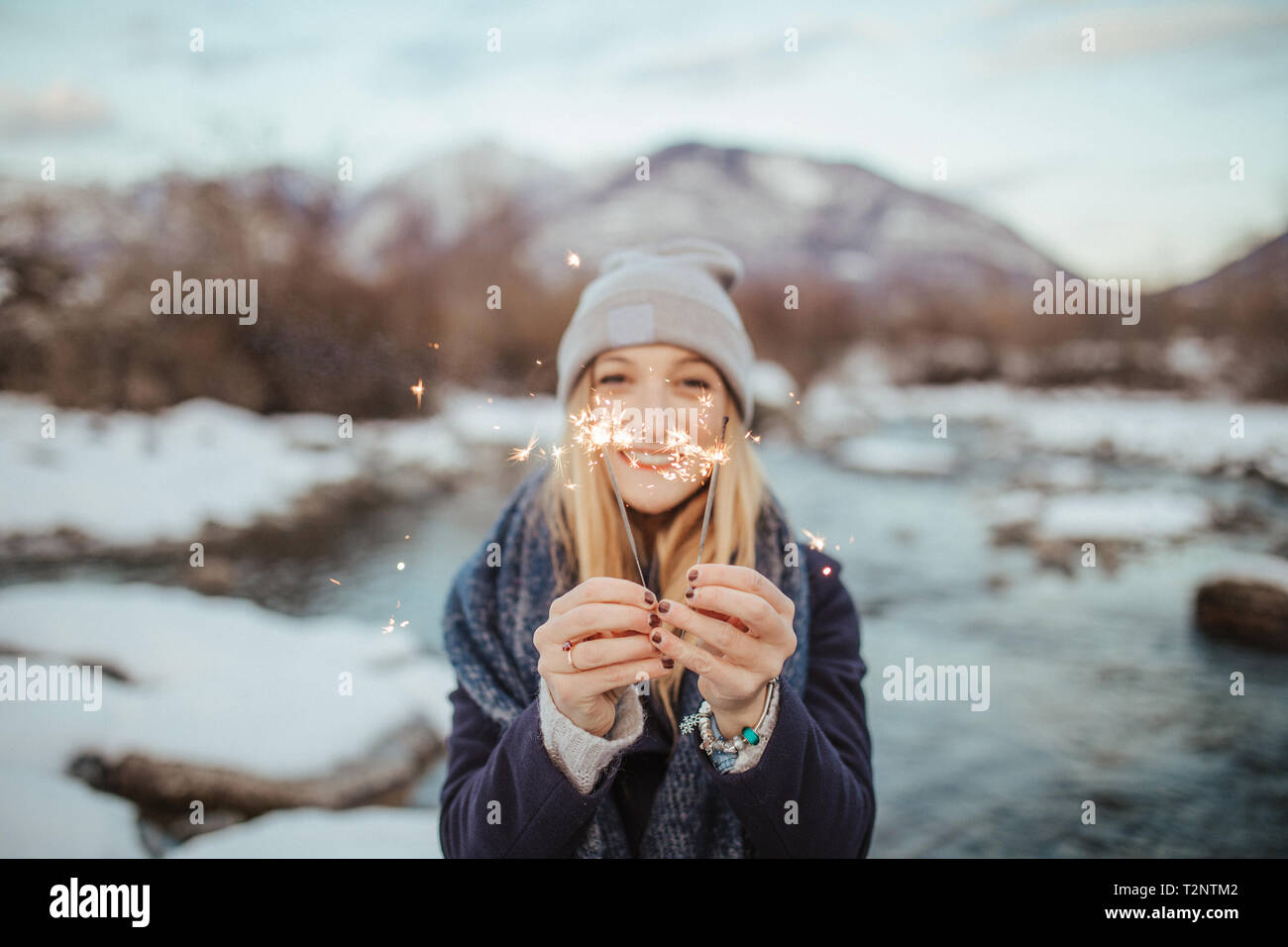 Femme au chapeau tricoté holding sparklers sur berges couvertes de neige, portrait, Orta, Piemonte, Italie Banque D'Images