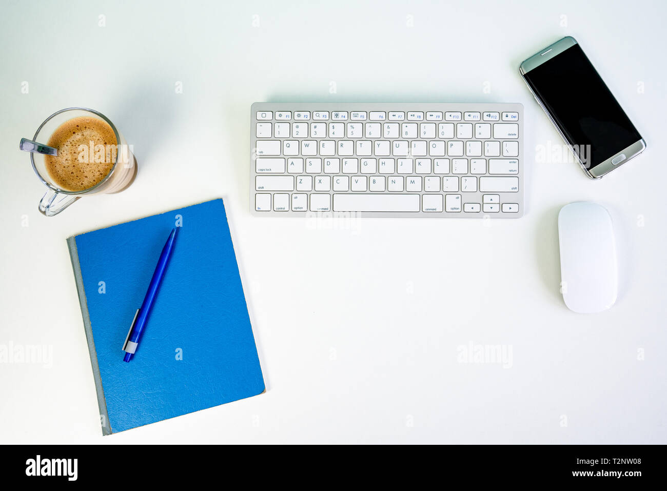 White Bureau bureau avec clavier, souris sans fil, smartphone, tasse de café, un crayon et un bloc d'écriture Banque D'Images