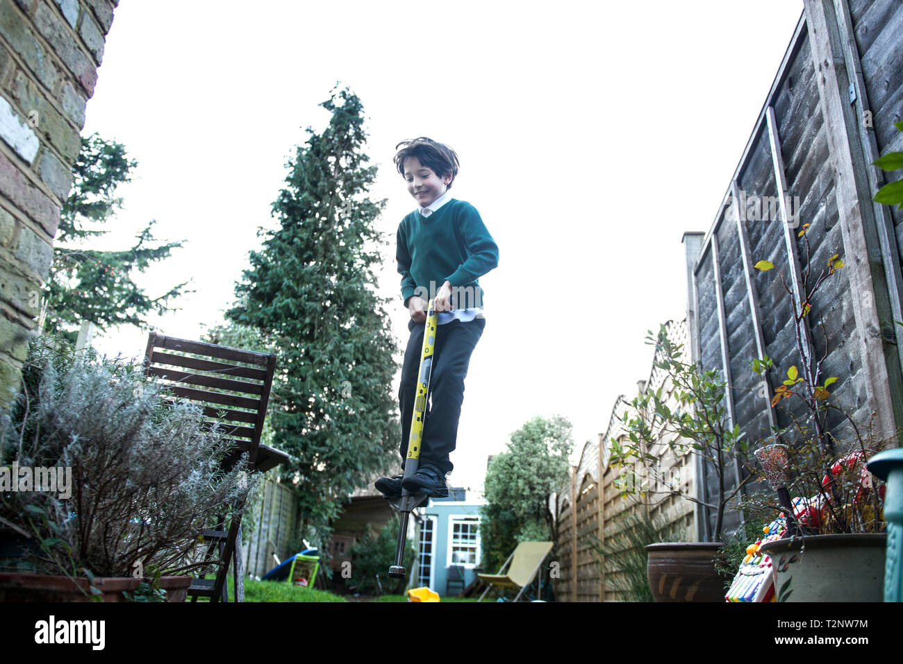 Garçon sautant sur un Pogo Stick in garden Banque D'Images