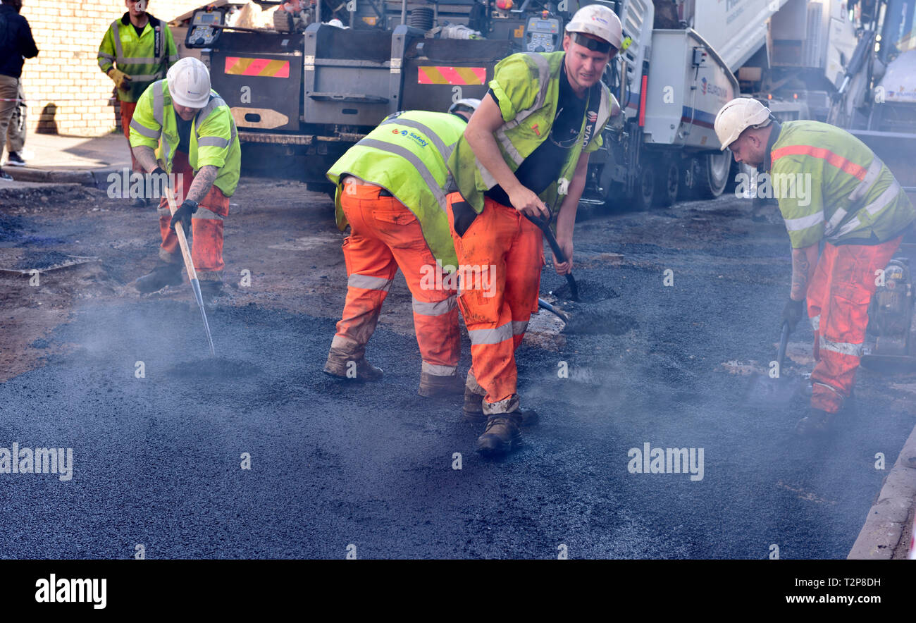 Équipe d'ouvriers à pelleter, la diffusion de Sex tarmac sur city road la réparation, England, UK Banque D'Images