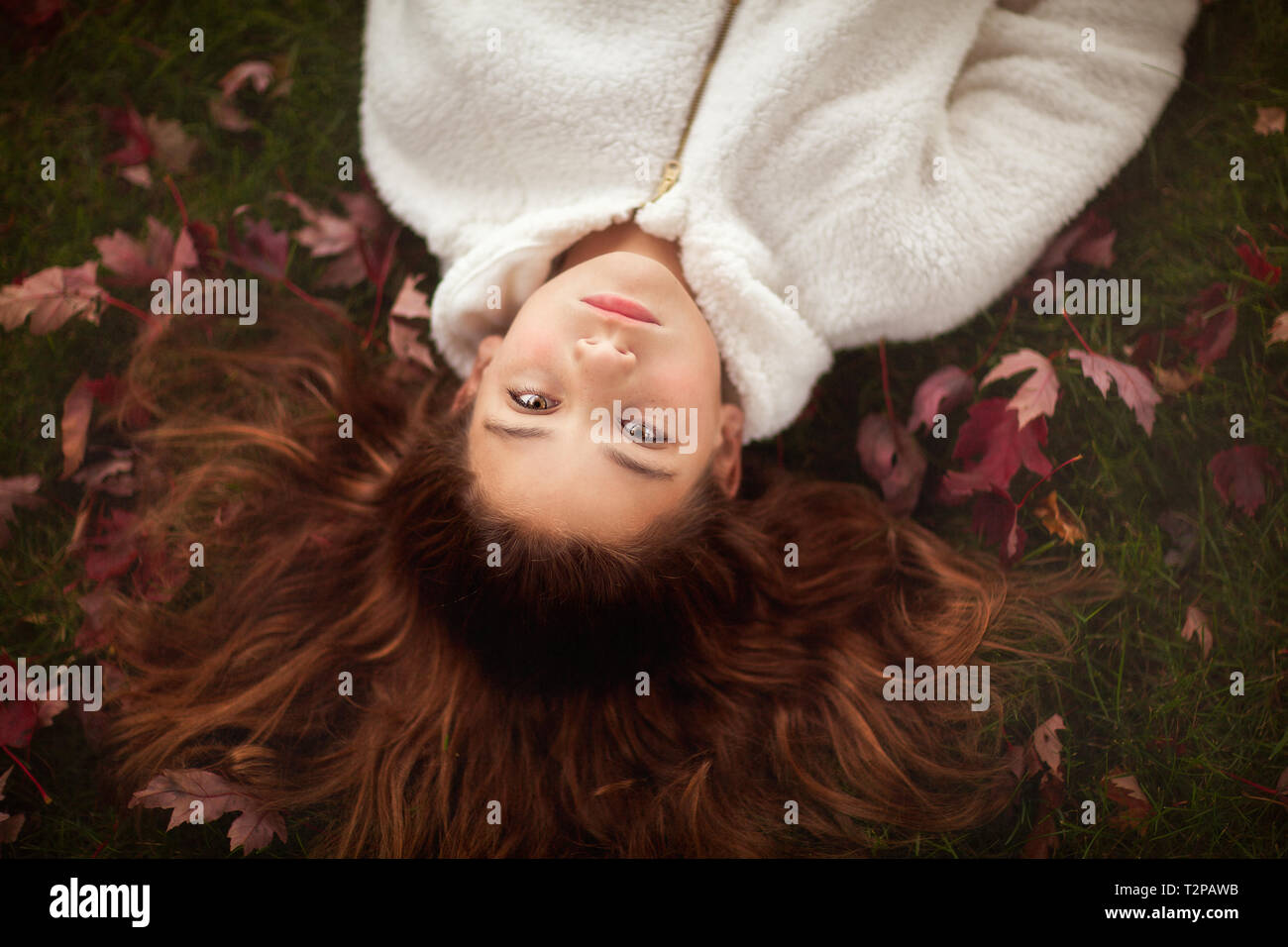 Fille aux longs cheveux auburn lying on grass parmi les feuilles d'automne, portrait Banque D'Images