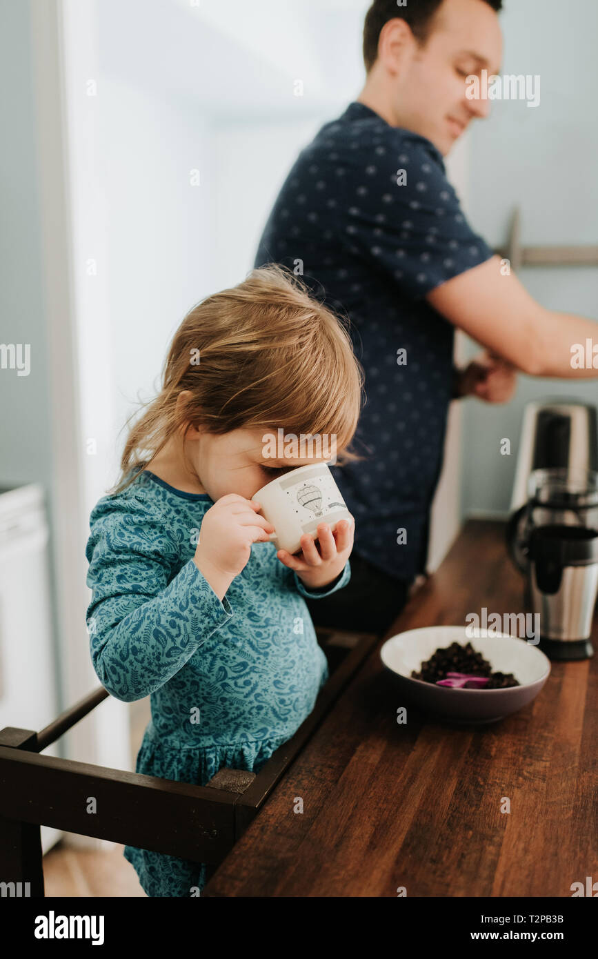 Female toddler avec père de boire à la coupe du comptoir de la cuisine Banque D'Images