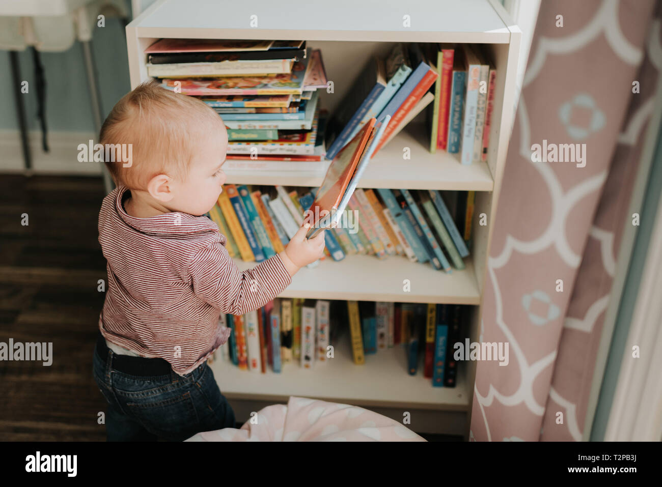 Bébé garçon dans la salle de séjour retrait livre d'histoires d'étagères Banque D'Images