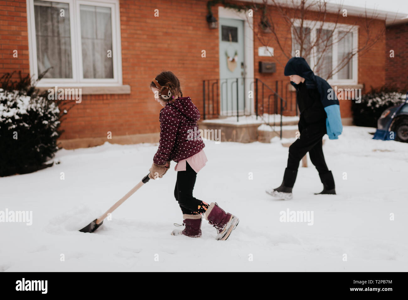 Les enfants de pelleter de la neige en face de la maison Banque D'Images