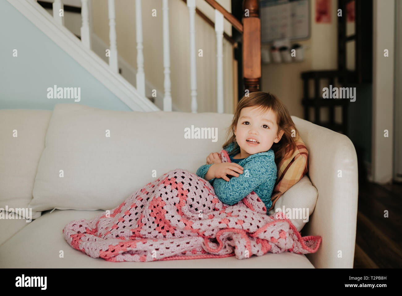 Female toddler sur canapé avec une couverture, portrait Banque D'Images